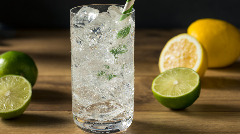 A glass of lemon-lime soda with fresh lemons and limes scattered around it