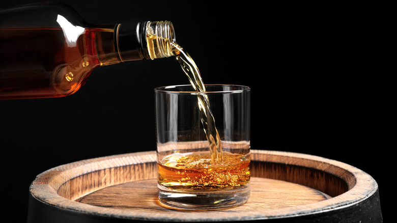 Pouring bourbon into a highball glass on top of a bourbon bottle