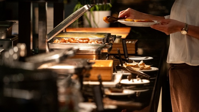 Someone serving themself with tongs at a restaurant buffet