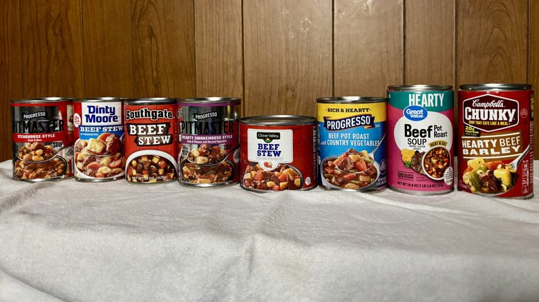 A row of canned beef stews on display, from left Progresso Pitmaster Steakhouse-Style, Dinty Moore, Southgate, Progresso Pitmaster Hearty Smokehouse-Style, Clover Valley, Progresso Beef Pot Road and Country Vegetables, Great Value Beef Pot Roast Soup, and Campbells Chunky Hearty Beef Barley