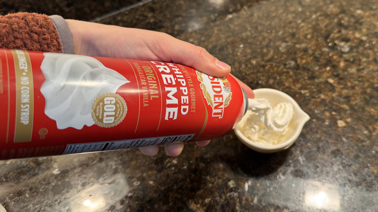 Person dispensing canned whipped cream into a small, white dish