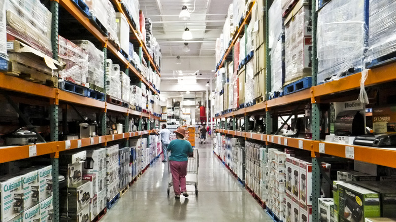 A Costco aisle with a person walking down it with a shopping cart, facing away from the camera.