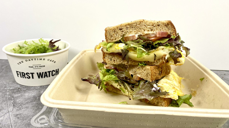 The First Watch BLTE in its to-go container next to a small side of salad