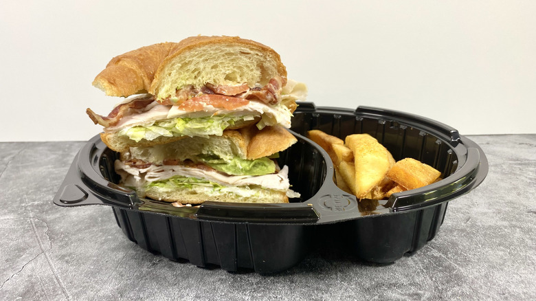 The Red Robin BLTA Croissant in its to-go container next to steak fries