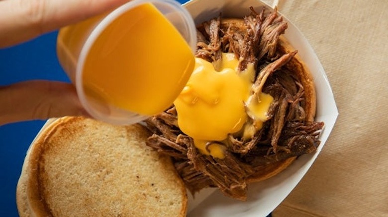 A person pouring cheese on a pot roast sandwich at Culver's