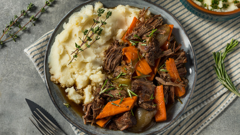 A plate of pot roast with vegetables and mashed potatoes