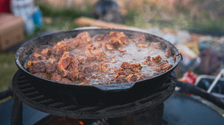 beef stew being cooked in cast iron pan over open fire