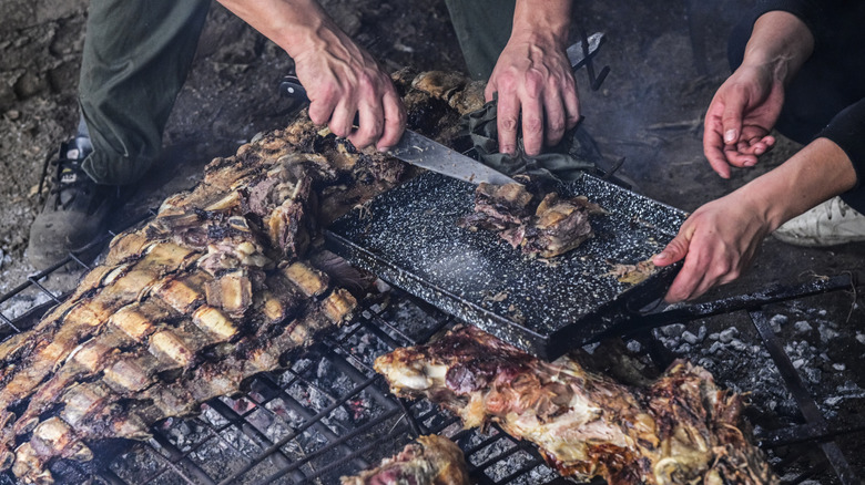 Hands removing beef ribs that have been cooked over an open fire