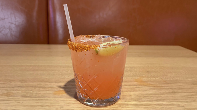 A watermelon margarita with Tajín rim sits on a wooden table.