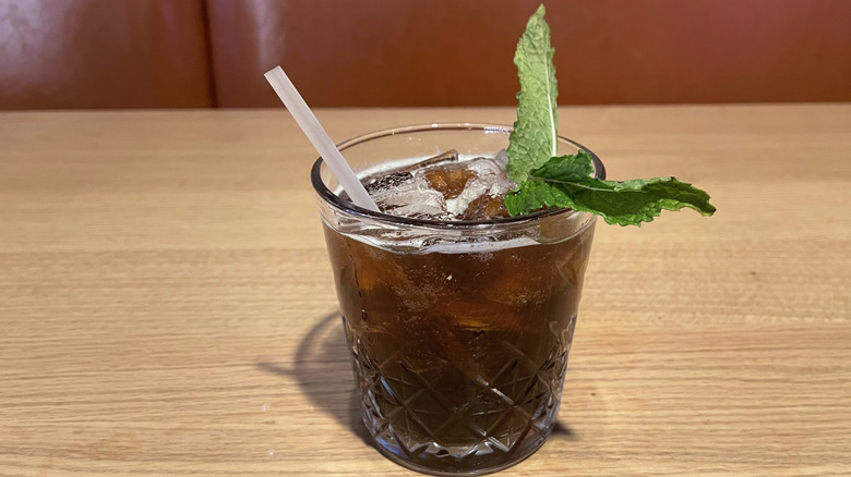A brown-colored drink with mint leaves sits on a wooden table.
