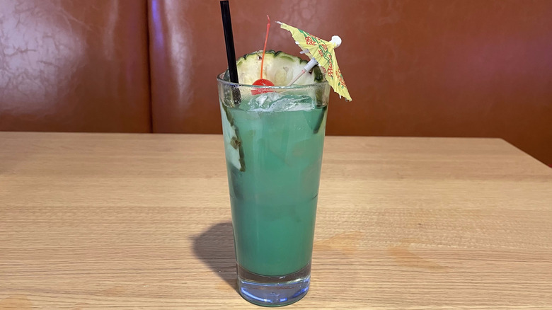A blue drink with an umbrella and pineapple slice sits on a wooden table.