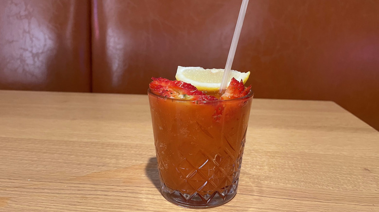 A cocktail with strawberries and lemon garnish sits on a wooden table.