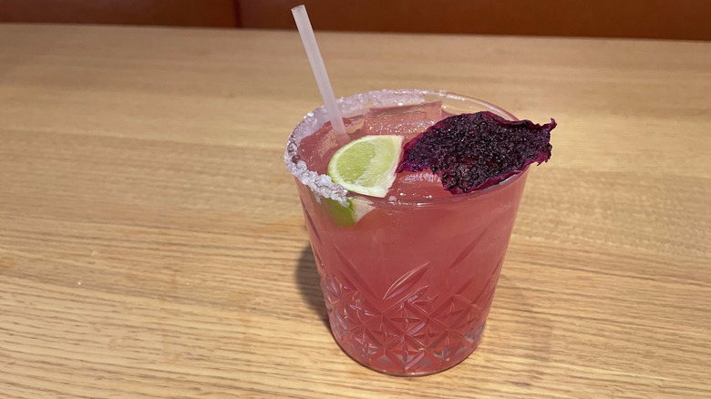 A pink margarita with a dragon fruit slice sits on a wooden table.