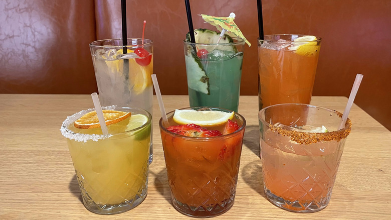 Six cocktails available at Dave and Buster's sit on a wooden table at a booth.