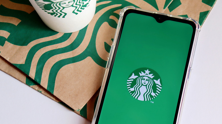 Phone with Starbucks logo from app, beside a takeout cup and paper bag