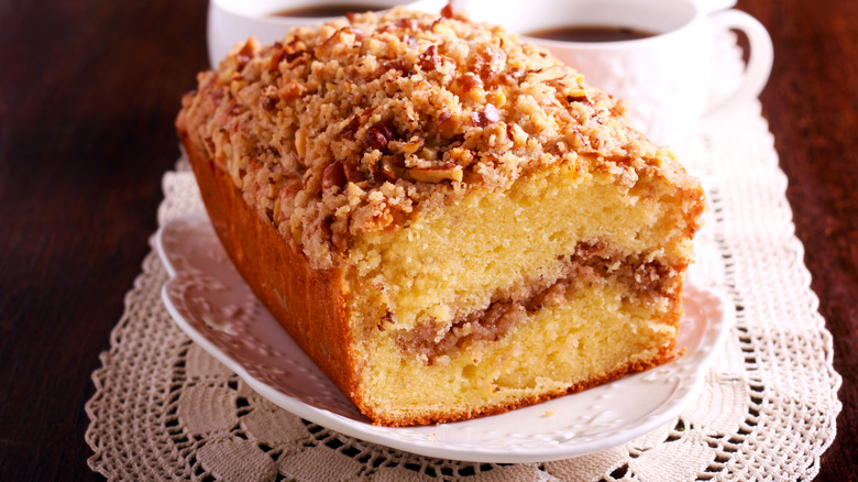 Coffee cake on a white dish with coffee cups in background