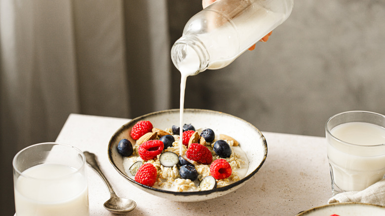 A person pouring milk into a bowl of fruit-topped oatmeal