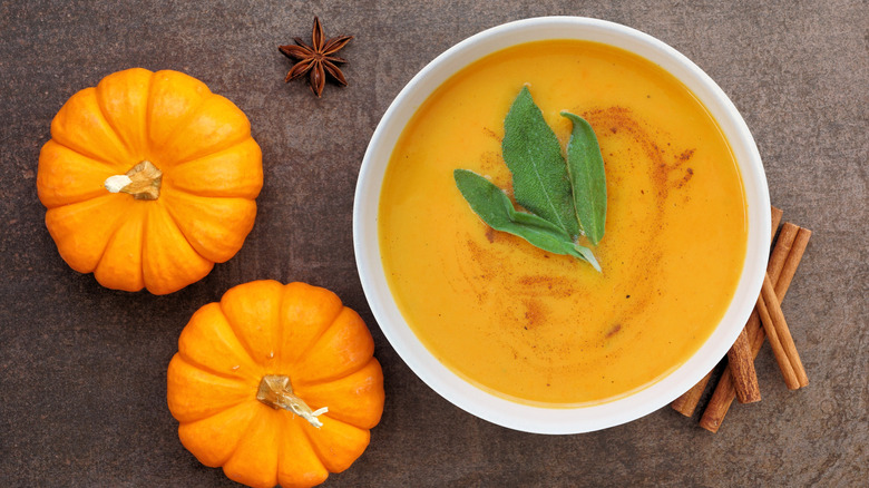 A bowl of cinnamon pumpkin soup with pumpkins and spices surrounding it
