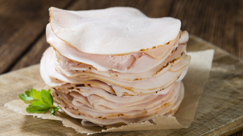 Thinly sliced chicken breast lunchmeat on wood cutting board.