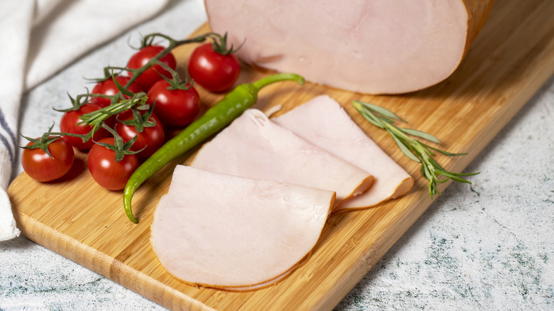 Smoked turkey slices on cutting board next to pepper and tomatoes.