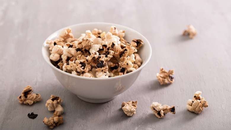 Partially burnt popcorn in a white bowl, with popcorn pieces around the outside