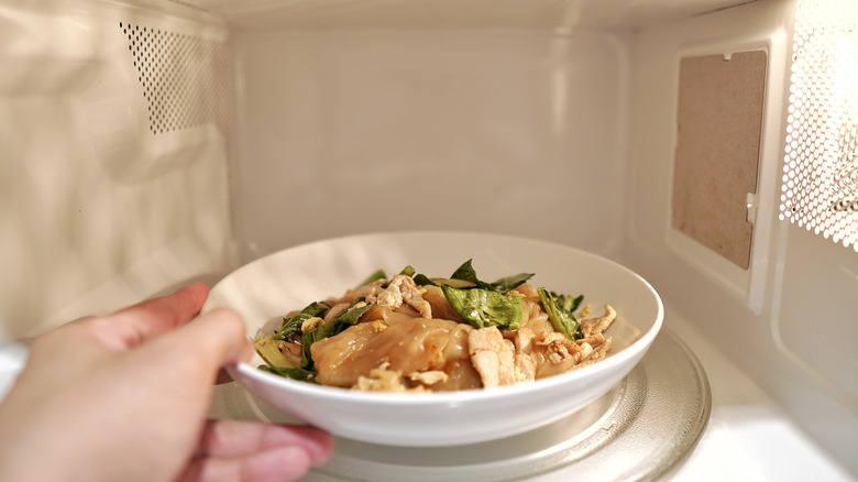 Person's hand rotating bowl of food in microwave