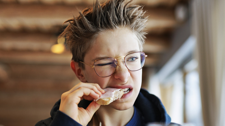 Person struggling to bite into stale bread with meat on top