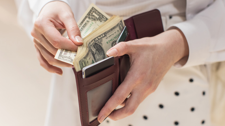 A person's hands taking dollar bills out of a brown leather wallet