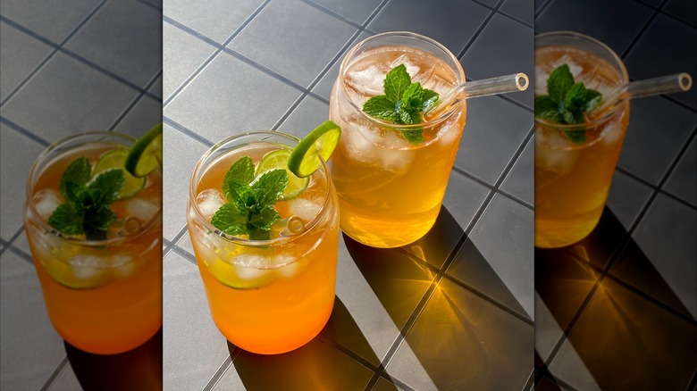 Two glasses of citrus mint iced tea on a gray tile background