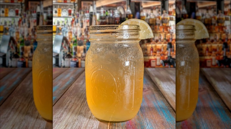 A John Daily in a mason jar with a lemon on the rim on a wooden table