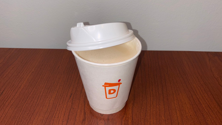 A very light tan chai latte in a Dunkin' to-go cup with the lid half off showing the liquid inside.