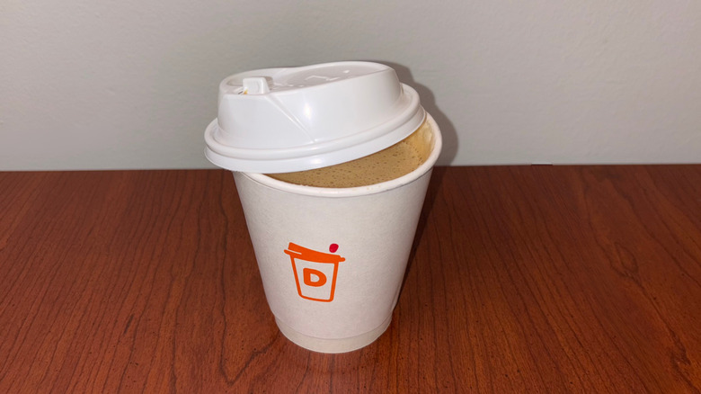A medium brown, foamy latte in a Dunkin' to-go cup with the lid half off showing the liquid inside.