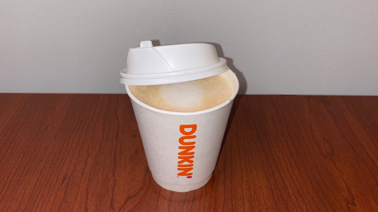 A light, foamy latte with white foam ring in the middle of a Dunkin' to-go cup with the lid half off showing the liquid inside.