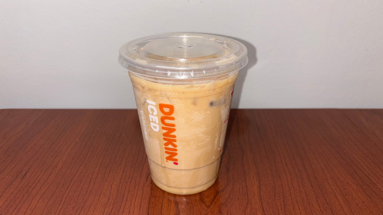 A tan iced coffee in a clear plastic Dunkin' to-go cup with condensation trails on the cup