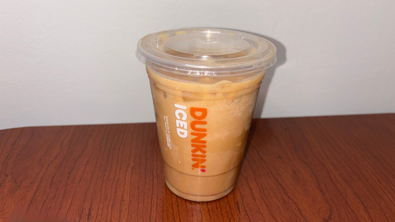 A medium light brown iced coffee in a clear plastic cup has condensation on the surface.