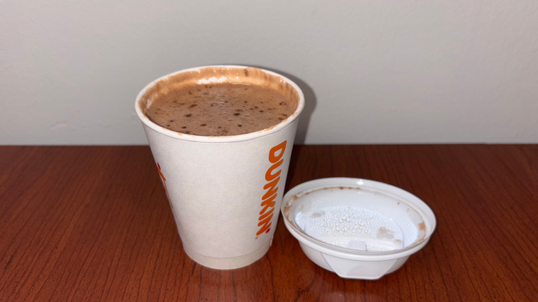 A hot chocolate in a Dunkin' to-go cup with the steamy lid upturned next to it.
