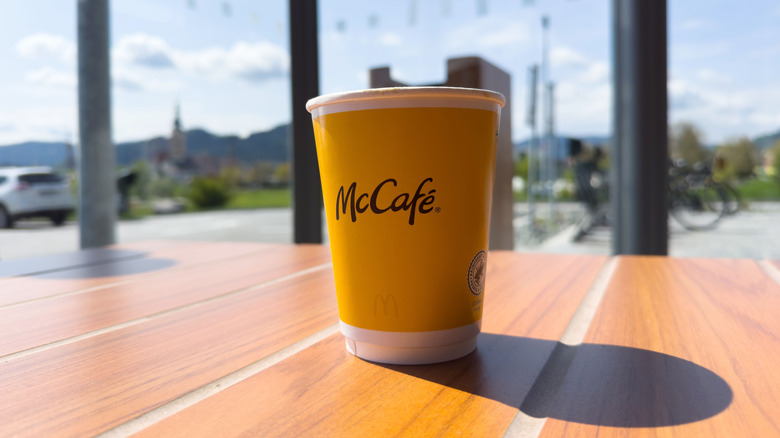 McCafe coffee cup prominently displayed on a wooden table, sunlight illuminating the scene.