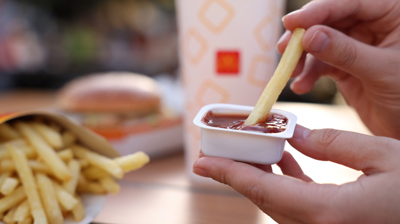 A close up of someone dipping a french fry into a McDonald's dpping sauce