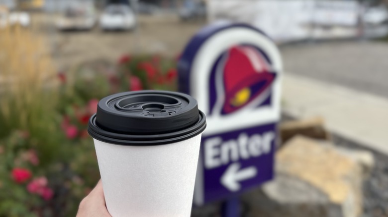 hand holding coffee cup in front of Taco Bell sign