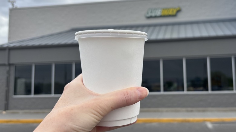 hand holding cup of coffee in front of Subway sign
