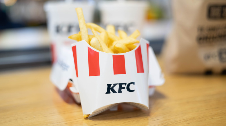 Carton of KFC fries with a sandwich and drink in background