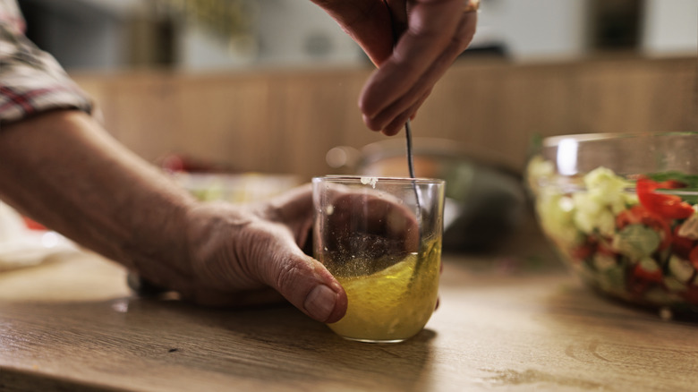 Someone preparing a homemade salad dressing by stirring olive oil and vinegar in a glass