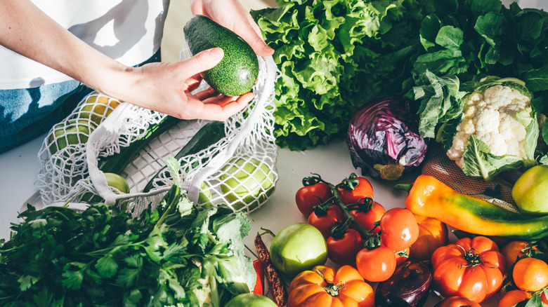 Someone gathering veggies in woven tote bag