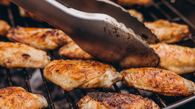 Chicken wings being cooked on grill with tongs nearby