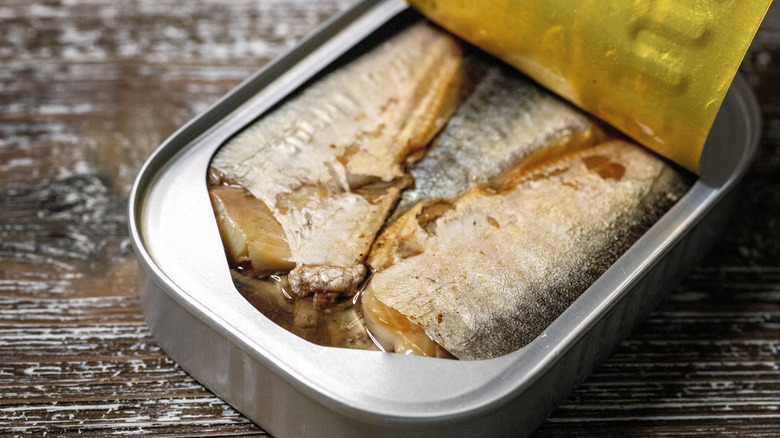 A half opened can of sardines on a wooden background