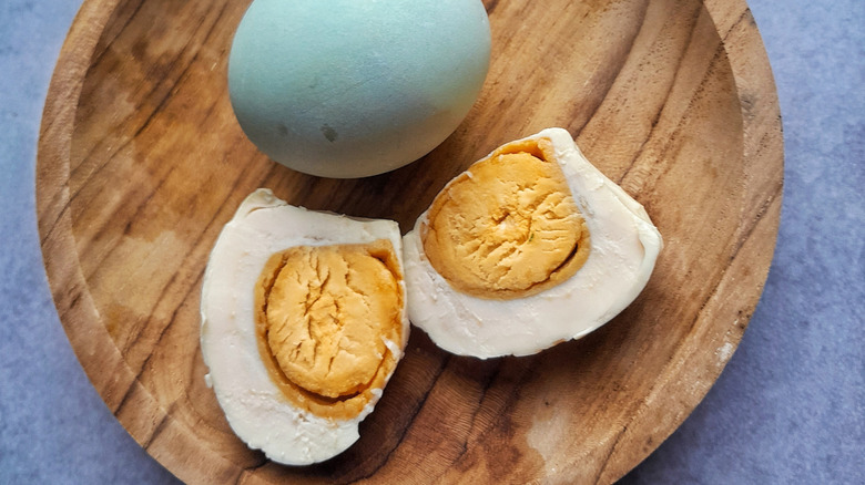 boiled egg split in half and a full egg on a wooden plate