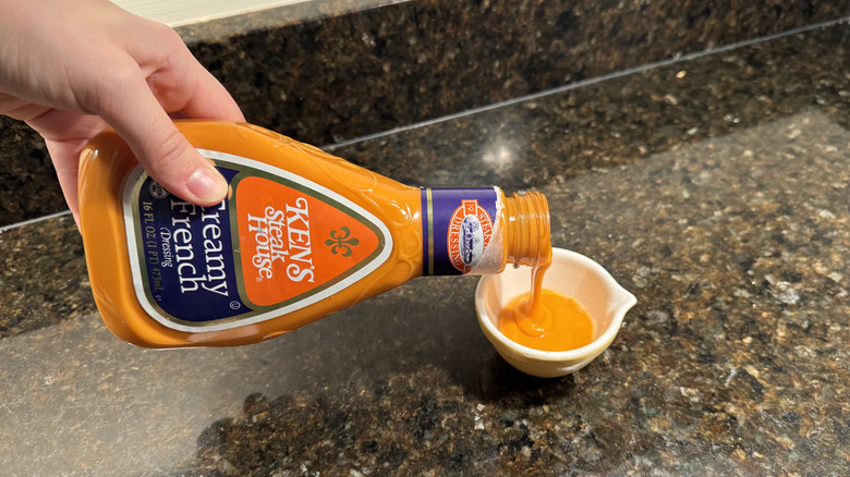 A hand pours creamy French dressing into a small white dish