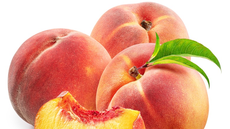 A slice of peach sits in front of three whole peaches