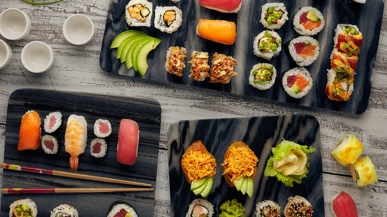 a variety of sushi rolls spread out on a black platter