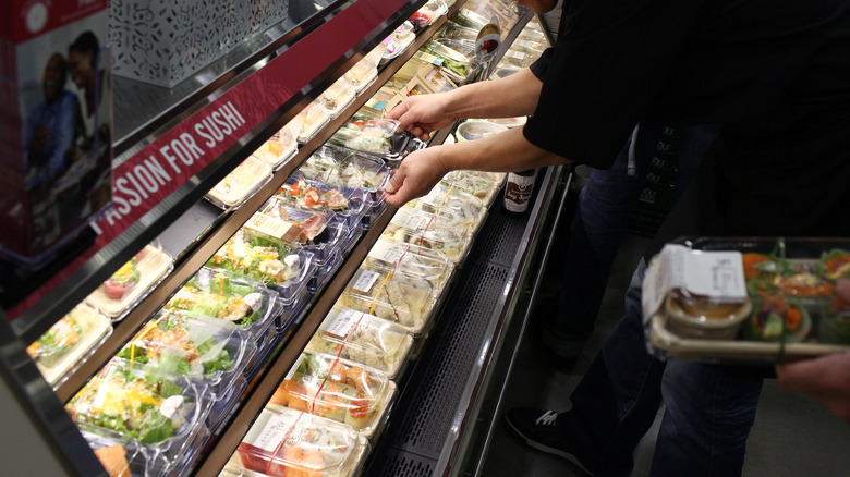sushi chef placing packaged sushi rolls into the fridge at Whole Foods